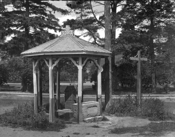 View of a roof-covered water pump in a wooded residential area.