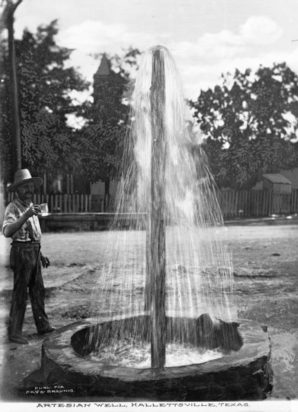 A man with a small glass or cup stands next to an artesian-style well spouting water. Caption reads: "Artesian Well, Hallettsville, Texas."