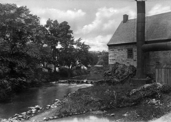 Exterior photograph of the first water works in America, consisting of a stone cottage next to a stream.