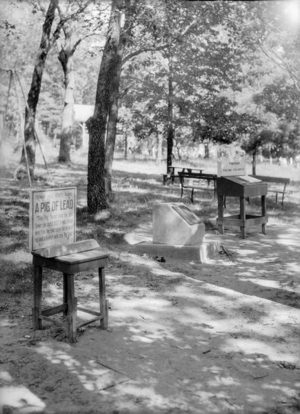 An outdoor exhibit, possibly at Tower Hill State Park, with a display featuring a "pig of lead" found near the shot tower there. There is also a bronze plaque on a monument and a visitor log. There are picnic tables and a small shelter in the background.
