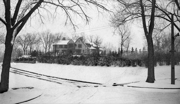 An imposing Tudor style stone and stucco house sits on a large wooded lot. There is a decorative fence and hedge along the driveway. The house was the home of E.P. McFetridge, president of the Island Woolen Mill.
