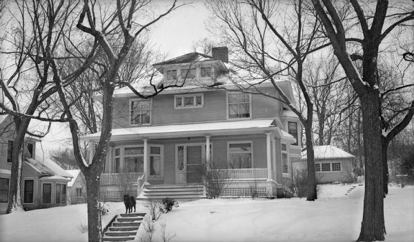 View from street of a dog standing on front walk in front of the Dr. Chris L. Thuerer home, a large Four Square Style house which has large bay windows and a columned front porch.