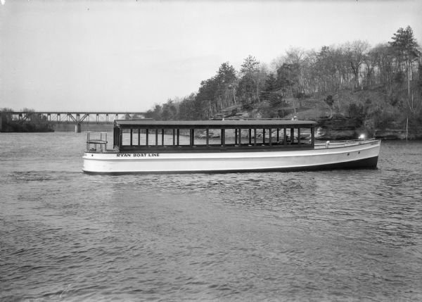 The tour launch <i>Seagull</i>, of the Ryan Boat Line, on the Wisconsin River at the Dells. The Kilbourn bridge is in the background.  The captain is the only person aboard.