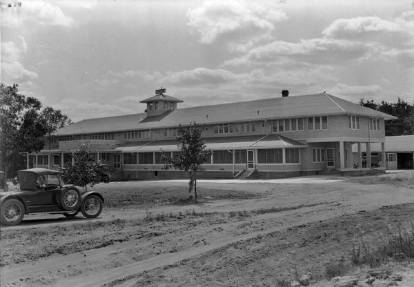 Several cars are parked on the unpaved drive of the two-story Hotel Morris at Lake Delton.  There is a porte cochere on the right and a large garage to the rear of the building.