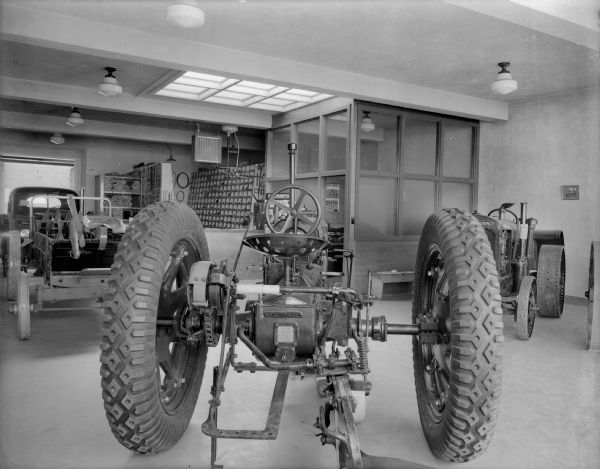 A clean and well lit International Harvester showroom with two tractors, a manure spreader and pickup truck. The Farmall tractor in the foreground has rubber tires, which were first introduced for tractors in 1932. The McCormick-Deering tractor against the wall has older style metal wheels. There is an ox yoke on the manure spreader.