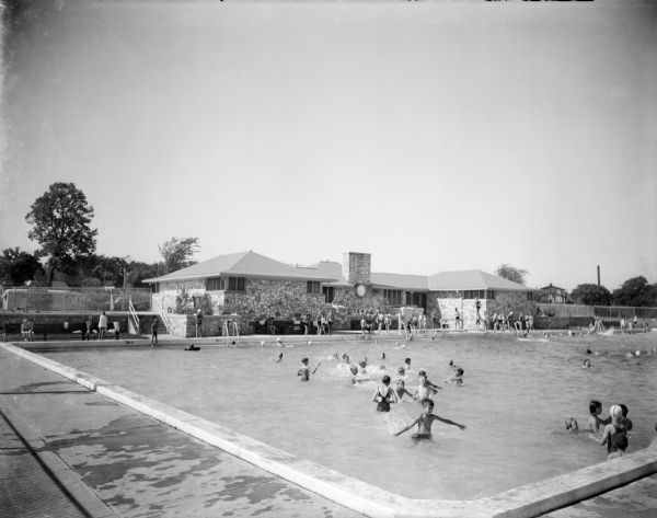 Children play in a large swimming pool with a stone changing house.