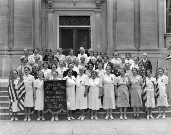 A group of women stand on the steps of the Sauk County Courthouse. A banner identifies them as the Department of Wisconsin, National Daughters of the G.A.R. (Grand Army of the Republic).  The organization was founded in 1907; its members were female "direct lineal descendants" of Civil War (Union) veterans. The group disbanded in the late 1970's.