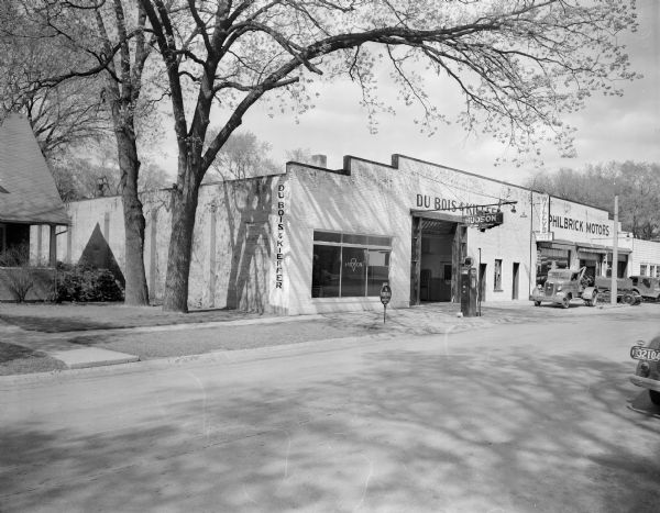 The Du Bois and Kieffer Hudson dealership, and Philbrick Motors, a Willys dealership, which shared a building at 137 Third Avenue. There is a Phillips 66 gas pump and a sign for Kendall Oil in front of the Hudson portion of the building. A tow truck, canvas covered trailer, and Jeep are parked in front of the Willys dealership.