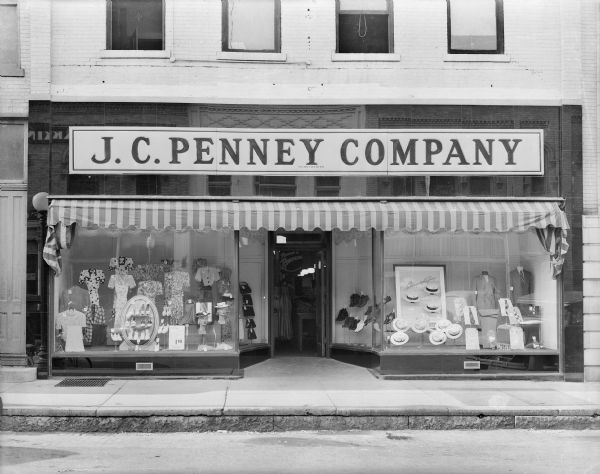 The storefront of the J.C. Penney store, 127 Third Street. There are summer clothes, hats, and shoes for men and women in the display windows. There is a highly reflective material around the storefront in which the buildings opposite can be seen. A sign inside the front door announces that "Penney's is Remodeling."