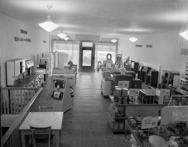 Elevated view of the interior of Ryan Hickethier & Co., a "Sears Associated Store" 132 Fourth Avenue. Kenmore appliances, Silvertone radios, and floor sweepers are displayed. There is a selection of oil burning heaters, in addition to Prestone anti-freeze and hardware.