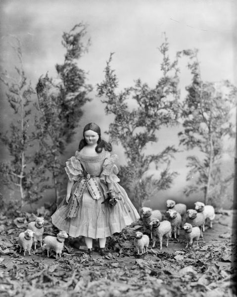 A doll from the collection of Alice Kent Trimpey is posed with a flock of toy sheep.