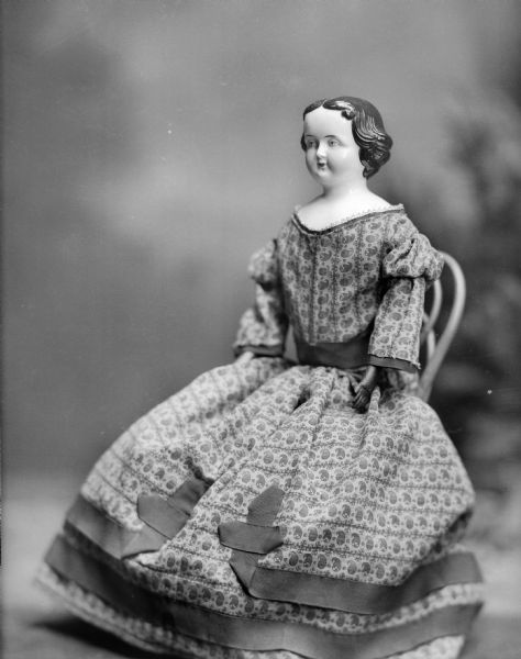 A doll named Becky, with china head and old-fashioned dress, sits on a small chair.