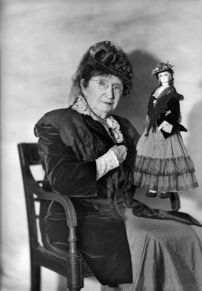 Mrs. Trimpey sits in a chair holding her doll, Emeline.
