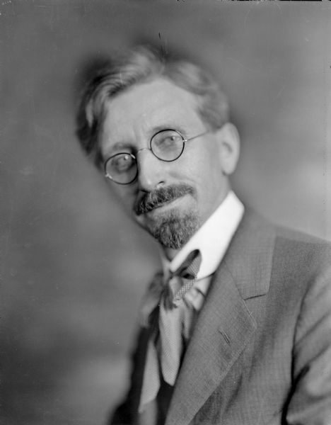 A studio self-portrait of Ephraim B. Trimpey with goatee, wearing eyeglasses and a large cravat.