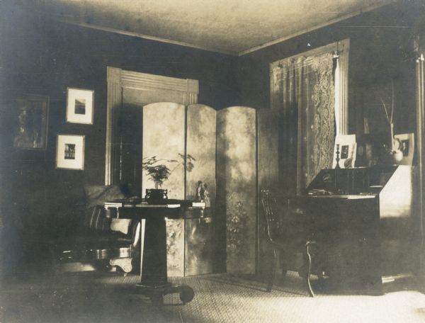 Interior view of the home of the photographer, including a four panel screen, open secretary desk, and small round table.