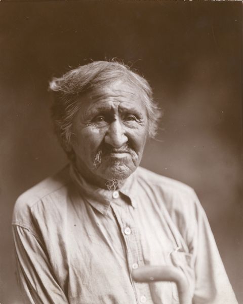 Head and shoulders portrait of an elderly Native American man. He is wearing a work shirt; the handle of a cane is in the foreground. On the reverse is written "Smoke Smoke, Winnebago."