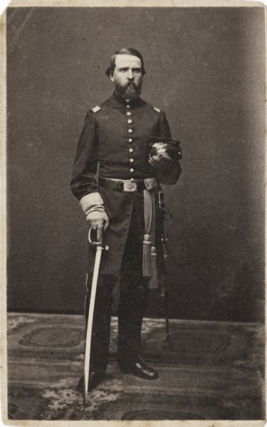 Full-length carte-de-visite portrait of 2nd Lieutenant Charles J. Robinson, Company G, 1st Wisconsin Infantry, standing with his sword in his right hand and his cap in his left hand.