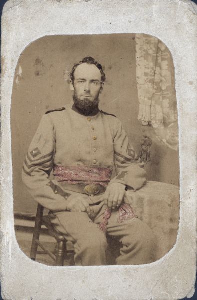 Seated carte-de-visite portrait of 2nd Lieutenant Emons Webster, Company B, 8th Wisconsin Infantry, in uniform. Webster nlisted in 1861 and survived the whole war. His uniform sash is hand-colored pink.
