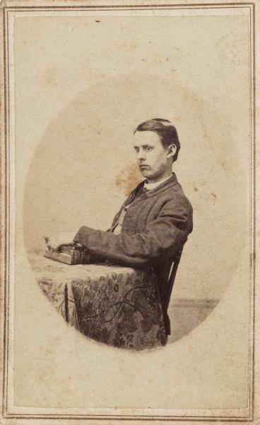 Seated carte-de-viste portrait of Thomas M. Heard (residence: Lorain County, Ohio), Company K, 2nd Ohio Heavy Artillery. He is sitting at a table with his hand on a book.