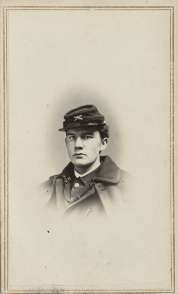 Vignetted quarter length carte-de-visite portrait of 2nd Lieutenant Alexander B. Keyes, 1st Battalion, Massachusetts Volunteer Heavy Artillery. He is wearing a hat and overcoat.