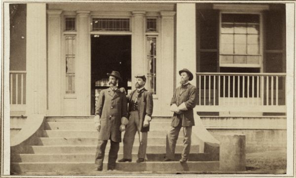 Three men standing at entrance of residence used as headquarters when S.G. Swain, (on left), was in charge of fortifications at Fort McPherson. All three men are wearing gauntlet gloves.