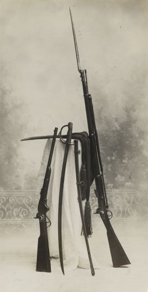 Captain George Nobles' weapons and sash used in the Civil War, posed in a studio in front of a painted backdrop.