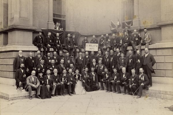 Group portrait of the members of the 11th Wisconsin Volunteers, and some family members, posed on the steps of what appears to be the old Milwaukee County Court House during a reunion.