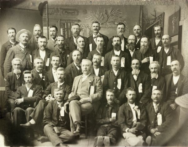 Studio group portrait of Union veterans gathered for the Grand Army of the Republic reunion. Colonel Rollin M. Strong, 19th Wisconsin Volunteer Infantry, is seated center front.
