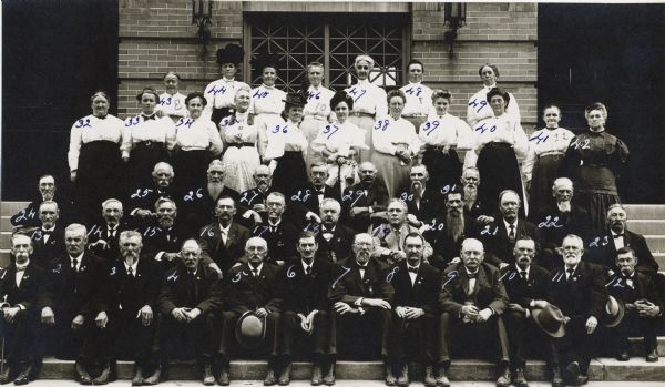 Group portrait of men and women at a Civil War reunion posed on the steps in front of a building. Those identified are 4) C. W. Sackett of Beloit 5) Herman Buchner, 7) Jacob Brant of Black Earth 9) Captain J.W. Hinkley, 13) Clinton W. Page of Waupun 19) Dr. Osborn, 20) Colonel G.W. Stevenson of Company F and S of the 3rd Wisconsin Volunteer Infantry 24) Bradley M. Bucklin of Janesville 26) Lawrence Post of Company K of the 3rd Wisconsin Volunteer Infantry 28) Mr. Schulte, 29) James Driver of Darlington, 30) William C. Meffert of Arena, and 31) W. B. Smith of Beloit. Captain Hinkley was with Company E, 3rd Wisconsin Volunteer Infantry during the Civil War.