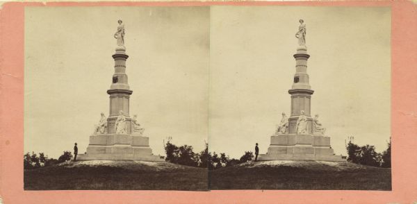 Stereograph of a monument in the Soldiers' National Cemetery at Gettysburg. A man is standing at the base of the monument on the left.