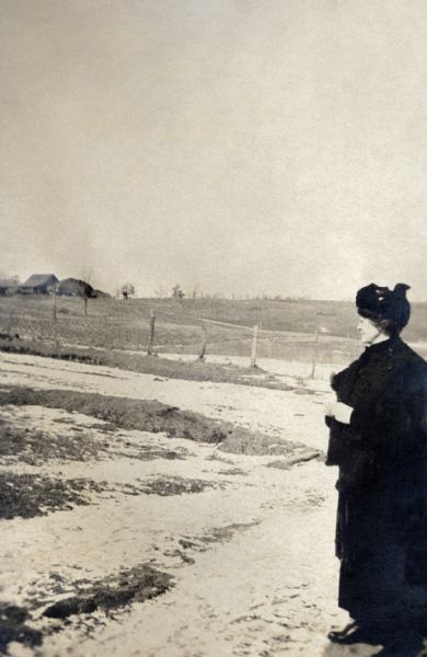 Katherine (Kate) Quinney, Richard Quinney's great aunt, standing on a country road near the family's farm looking over fields lightly dusted with snow.  The family's farmhouse is visible in the distance.