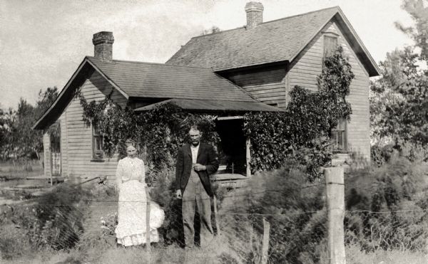 Thomas (Tom) and Florence Quinney standing in front of their farmhouse which has a climbing vine growing on it.