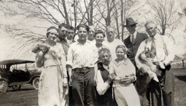 Family portrait taken in the yard of the Reynolds' farm with a Model T-Ford in the background. Left to right: Marjorie Quinney, William Henry Reynolds, Floyd Quinney, Millard Reynolds, Lettie Miles Reynolds, Fannie Smith Reynolds, Mary Quinney Reynolds, unknown man in hat, Matthias (Mate) Reynolds. In front are Wilbur James Reynolds and Marion Reynolds. 