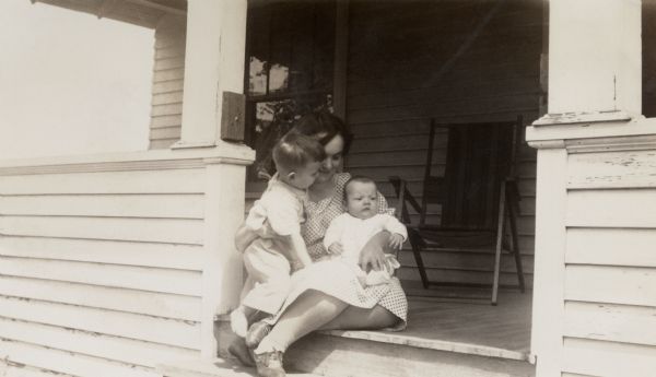 Richard Quinney and his new brother Ralph held by their mother on the front porch of the farmhouse.
