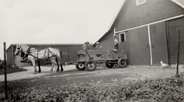 Richard and Ralph Quinney with their father, Floyd Quinney, riding in the back of a horse-drawn grain wagon in the farmyard.