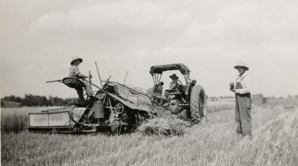 Young Ralph and Richard Quinney pose for a picture while they cut grain by themselves for the fist time.  View includes a grain binder, a tractor and their father, Floyd Quinney, standing alongside.