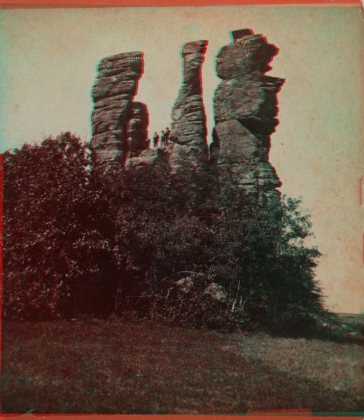 Three men standing atop a large rock formation. Caption on back of stereograph reads: "Three Chimneys 3 miles S. of Viroqua, Wis."