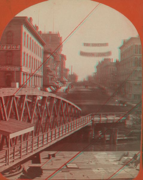 Stereograph of Wisconsin Street seen from Spring Street. The building on the left nearest the bridge was the Chicago, Milwaukee & St. Paul Railway's downtown office. The banner above Wisconsin Street reads "For Governor Harrison Ludington".