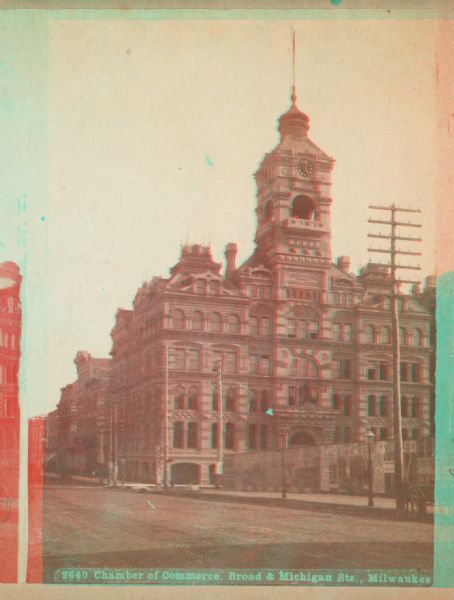 Stereograph view of Chamber of Commerce at Broad and Michigan Streets.  The building is the center of the image, with a telephone pole to the right, a large fence in front of the building, and a cart next to a street.