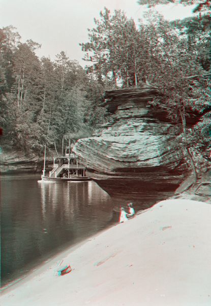 Stereograph of the steamboat the "Dell Queen" at Chapel Gorge. A woman and a young child are sitting on the shoreline.