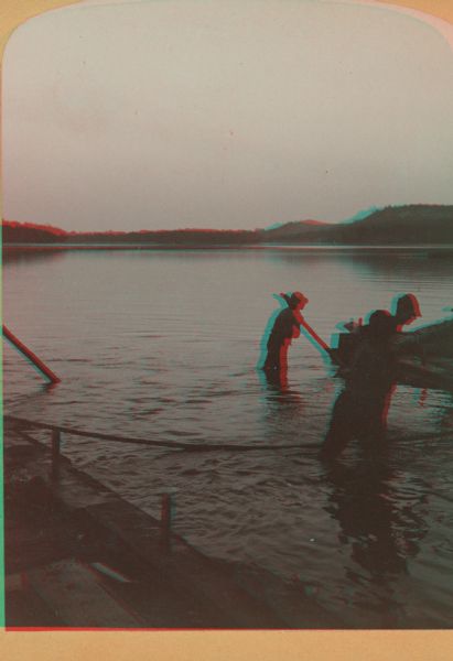 Stereograph of several men working at dusk, knee deep in water attending to the raft.