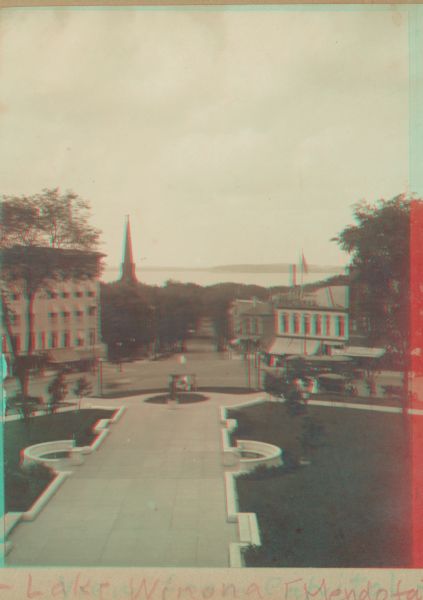 Stereograph view looking down State Street from the State Capitol during the construction of the fourth capitol building. The image features the Capitol Square sidewalk leading down toward State Street businesses. Lake Mendota is on the horizon.