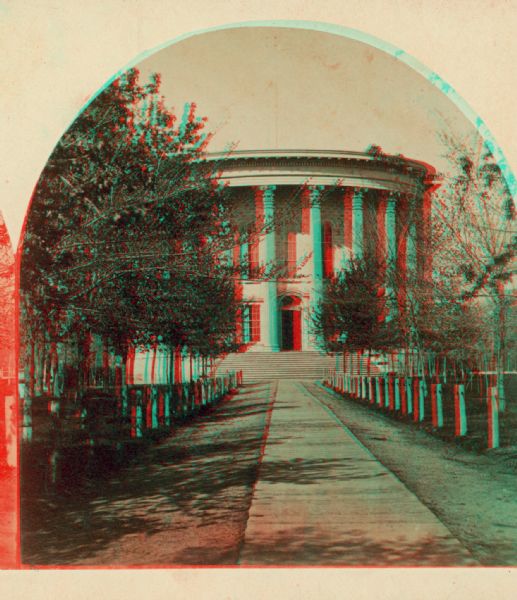 Stereograph view of the East Wing of the 2nd Wisconsin State Capitol built in Madison, also showing the pathway to the door then considered to be the front door, and trees in the Capitol Park. No identical view is included with Fuller's carte-de-visite format views of Madison.