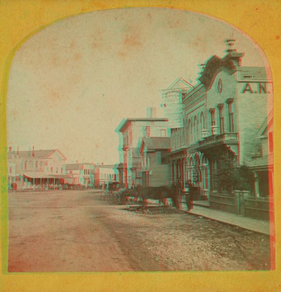 A stereograph of the town square and Main Street. The three-story building visible in the center of the photograph was operated as the National Hotel. It was later burned down and was replaced by the Menasha Hotel.