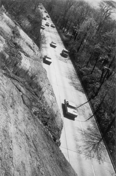 Elevated view from steep hill of vehicles traveling on the tree-lined Henry Hudson Parkway.