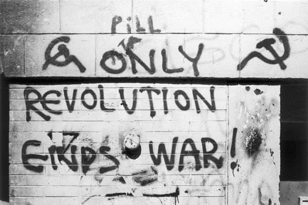 Close-up of a graffiti painted wall that reads, "Pill" and "Only Revolution Ends War!" framed by hammer and sickles.