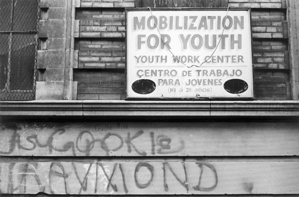 Close-up of a weathered stone facade with a framed sign that reads, "Mobilization for Youth, Youth Work Center, Centro de Trabajo Para Jovenes (16 a 21 anos)."