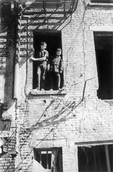 View from below of two boys standing in a doorway opening of an abandoned brick building in the East Village.