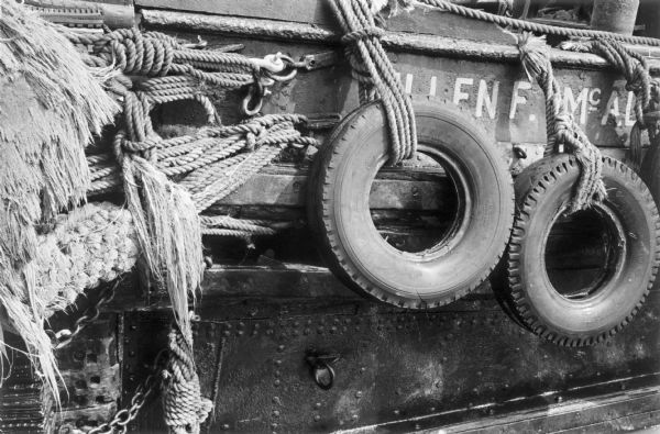 Close-up of the hull of a tugboat in the East River showing rigging, bumper-tires and part of the boats name, "-EN F. McAL-."