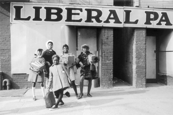A group of five girls holding school books pose for a portrait in front of a building on Coney Island.